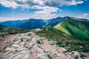 blue skies with white puffy clouds, green mountains and a curved rocky path