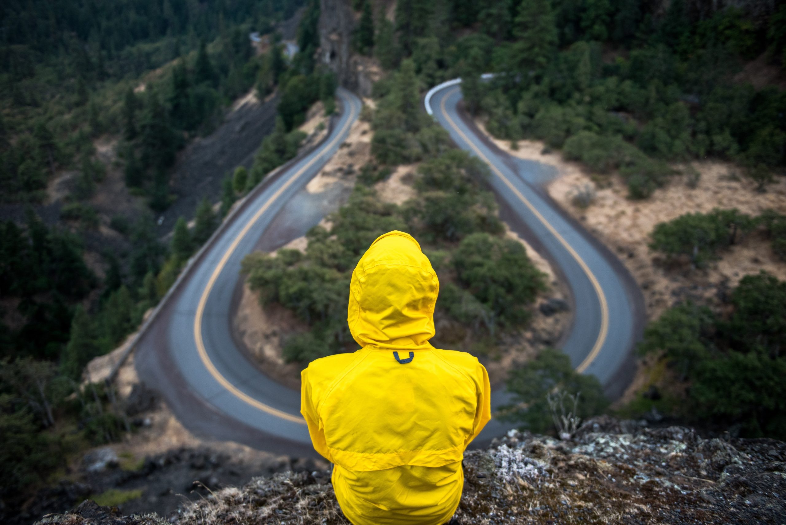 a person in a yellow hoodie facing away from us is watching an empty freeway from a height